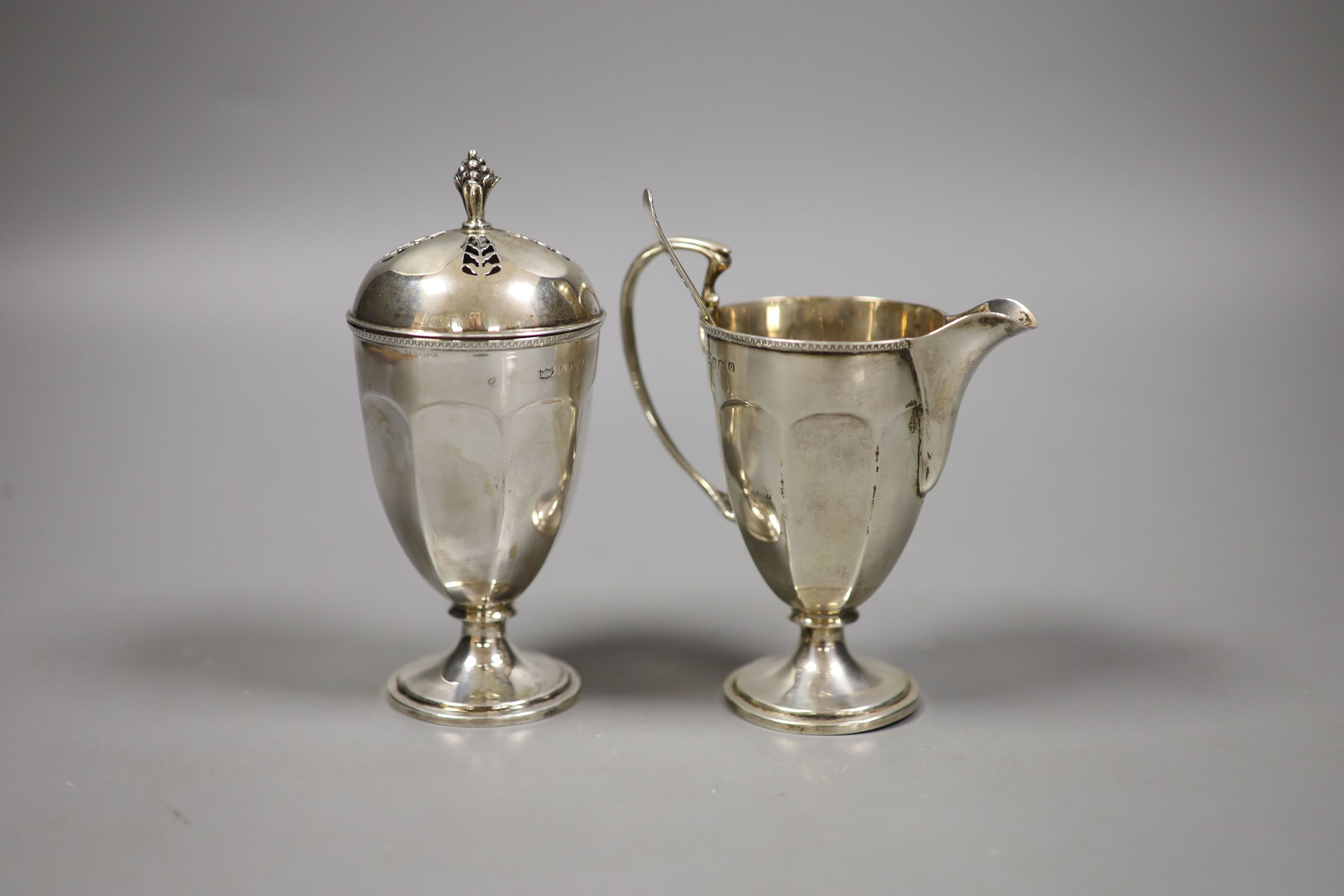 A George V silver helmet shaped cream jug, a silver sugar caster and a sifter spoon (3)